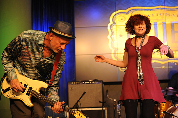 Rich McDonough plays guitar as Laura Green sings on stage.